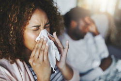 Woman blowing her nose and a man holding his head in pain