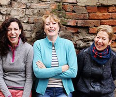 Three old women laughing, brick background