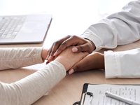 A physician comforting a patient by holding their hands 