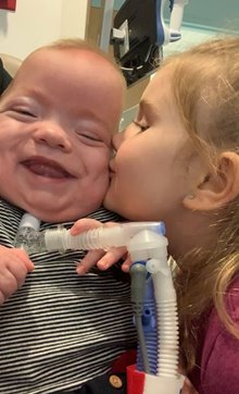 Ryder, a patient at Golisano Children’s Hospital of Southwest Florida smiling while receiving a kiss from his sister Kaylee.