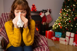 Woman blowing her nose with holiday decorations surrounding her