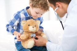 Little boy holding a teddy bear while the doctor listens to the teddy bear's heartbeat