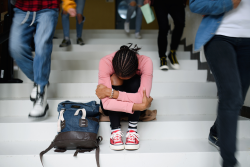 College student sitting on steps hugging legs. 